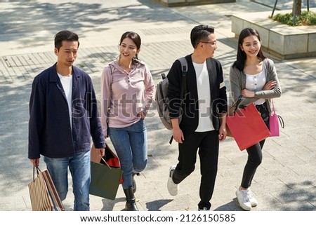 high angle view of group of four young asian people chatting talking conversing while walking on street with shopping bags in hands