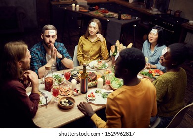 High angle view at group of friends playing guessing game while sitting at table enjoying dinner party in dark room, copy space - Shutterstock ID 1529962817