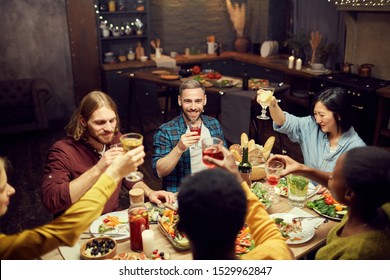 High Angle View At Group Of Friends Raising Glasses While Enjoying Dinner Together Sitting At Table In Dimly Lit Room, Copy Space