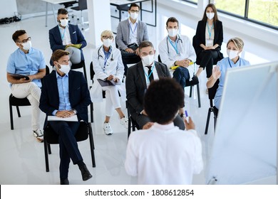 High Angle View Of Group Of Healthcare Workers And Business People Wearing Protective Face Masks While Attending A Seminar At Conference Hall. 