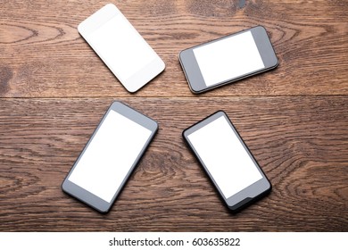 High Angle View Of A Group Of Mobile Phones Showing Blank Screen On Wooden Desk