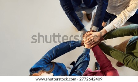 High angle view of group of multiethnic businesspeople stacking hands during business meeting. Close up of business hands of men and women giving high five in office. Top view of businesswomen and businessmen putting their hands together, celebrate project success, team huddle.