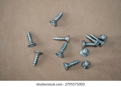 High angle view of a group of small metal screws scattered on a beige fabric background.Assorted metallic wood screws on a neutral textured surface. Carpentry and home improvement equipment.