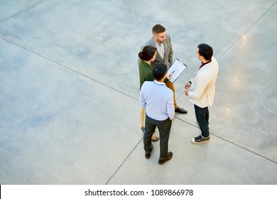 High Angle View At Group Of Successful Young Business People Standing In Circle Discussing Project In Modern Office Building, Copy Space