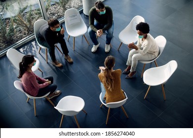 High angle view of group therapy participants sitting in a circle and talking while wearing protective face masks due to COVID-19 pandemic.