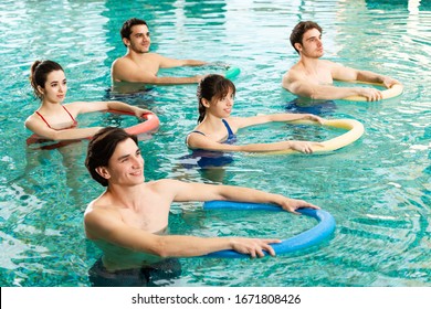 High angle view of group of young people holding pool noodles in swimming pool during water aerobics