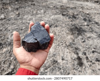 High angle view of hand holding black coal stone with ground background