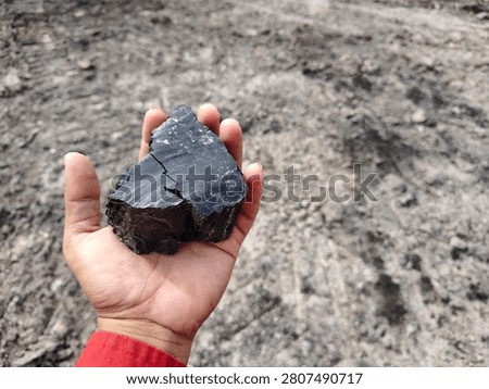 High angle view of hand holding black coal stone with ground background