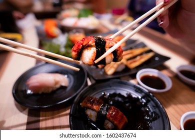 High angle view of hand serving Anago sushi together.Family eating and sharing Anago,maki,nigiri, uramaki.Top view, Group of people sitting with food, Top view of celebration party hands eating sushi.