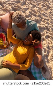 High Angle View Of Happy African American Mature Woman Lying On Senior Man's Lap On Sandy Beach. Romance, Fruit, Unaltered, Love, Togetherness, Retirement, Picnic, Enjoyment And Holiday Concept.