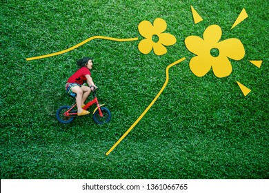 High Angle View Of A Happy Asian Kids. Girl On Bicycle Lay Down At Green Lawn In Spring Or Summer Day. Excited Asian Children In Outdoor Park