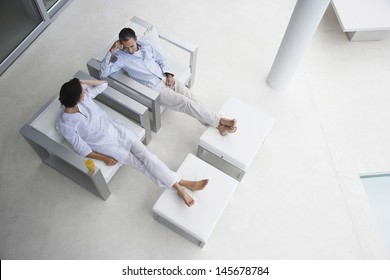 High Angle View Of Happy Couple Sitting On Armchairs With Feet On Foot Stools In Modern House