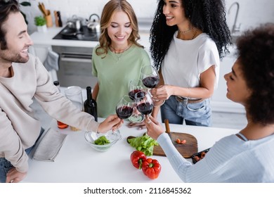 high angle view of happy multiethnic friends clinking glasses of red wine in kitchen