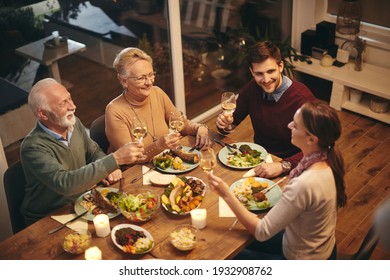 High angle view of happy senior woman toasting with her family while having a meal at dining table. 
