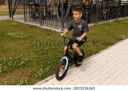 High angle view of happy smiling little boy riding bicycle on pavement next to green grass lawn in park during warm summer day active childhood lifestyle outdoor concept