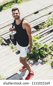 High Angle View Of Happy Sportsman Holding Bottle Of Water And Bag For Sport Equipment On Stairs At Sport Playground 