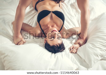 High angle view of happy tender cute smiling wife, husband gently are hugging under blanket in bed on dark bedsheet, man is kissing gently his woman in forehead