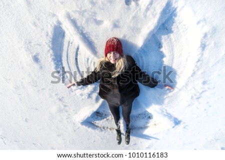 High angle view of happy woman lying on snow and moving her arms and legs up and down creating a snow angel figure. Smiling woman lying on snow in winter holiday with copy space. Top view