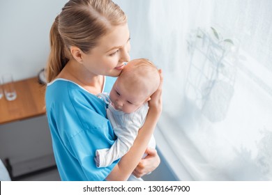 high angle view of happy young mother standing with adorable baby in hands and looking at window in hospital