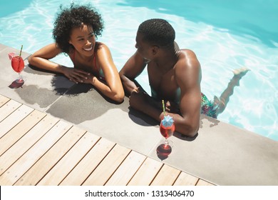 Vue en grand angle d'un jeune couple afro-américain heureux, assis au bord de la piscine dans leur jardin