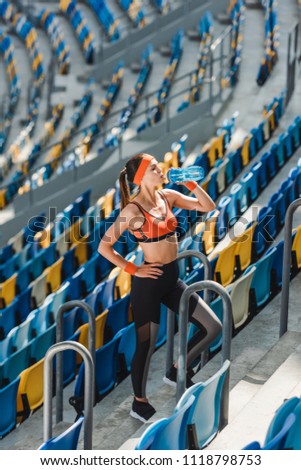high angle view of happy young woman drinking water on tribunes at sports stadium
