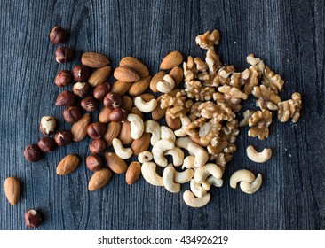 High Angle View Of Hazelnuts, Almonds, Walnuts And Cashews Scattered On A Black Wood Grain Background