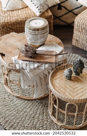 High angle view of home decor, wicker furniture with natural materials stand in bright living room interior at bohemian style. Vertical shot of bamboo table, candle and dry flower in cozy apartment