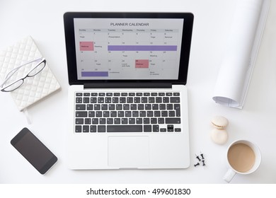 High angle view image of a working desk. Open laptop on the desk with a planner calendar on the screen. Business concept photo, close up