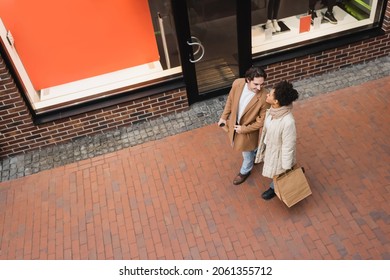 high angle view of joyful interracial couple with purchases walking in mall
