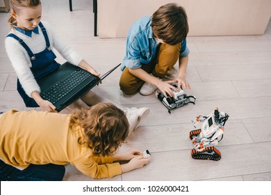 High Angle View Of Kids Sitting On Floor At Stem Education Class With Robots And Laptop