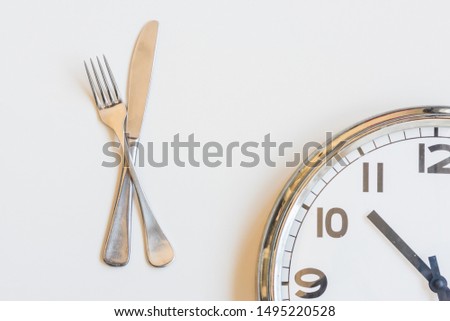 High angle view of knife and fork with clock on white background - intermittent fasting concept (selective focus)