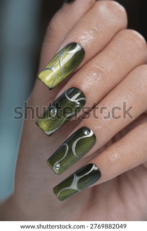 High angle view of long square nails showcasing olive green magnetic shimmer and creative embossed silver abstract designs