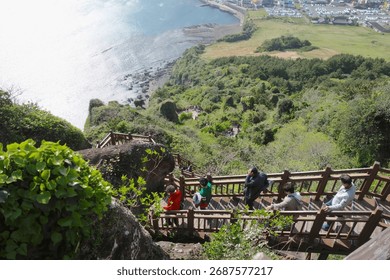 High angle view looking down steep, zigzagging wooden stairs with tourists descending from a volcanic peak to the coastal area below. Hiking and adventure concept.