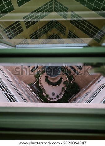 High angle view looking down through a window pane at an inner building courtyard with garden landscaping and a central structure.
