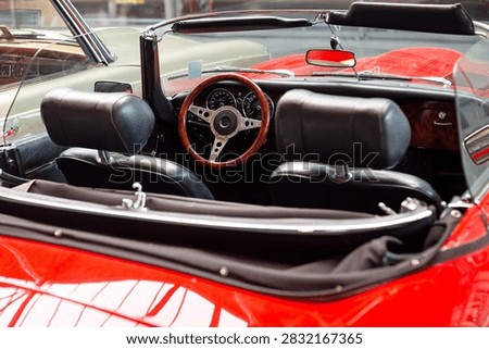 High angle view looking into the open cockpit of a red vintage convertible sports car showing black leather seats, wooden steering wheel, and dashboard.