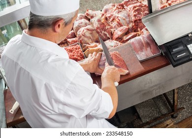 High angle view of male butcher cutting meat at display cabinet in butchery