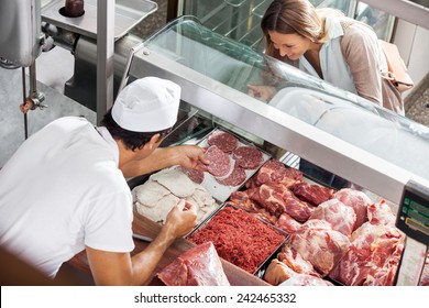 High angle view of male butcher showing meat to female customer at butchery