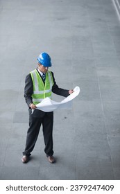 High angle view of an male Indian industrial engineer at work holding technical drawing plans.