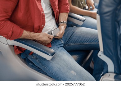 High Angle View Of Male Passenger Adjusting And Tightening A Seatbelt On An Airplane As He Pulls On The Belt With His Hands For Safe Flight. Safety, Traveling Concept