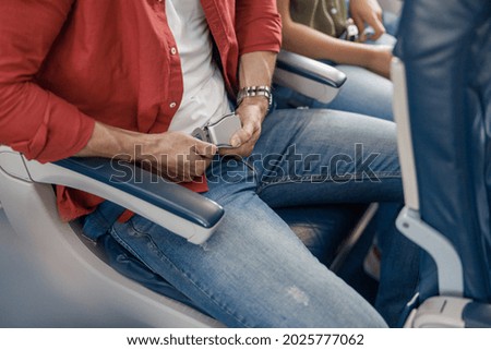 High angle view of male passenger adjusting and tightening a seatbelt on an airplane as he pulls on the belt with his hands for safe flight. Safety, traveling concept