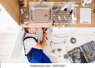 High Angle View Of Male Plumber In Overall Fixing Sink Pipe