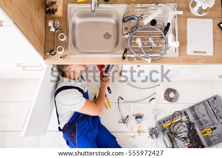 High Angle View Of Male Plumber In Overall Fixing Sink Pipe