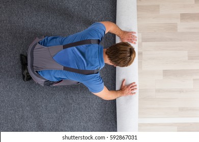 High Angle View Of Male Worker In Overalls Rolling Carpet On Floor At Home