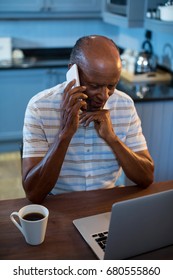 High angle view of man talking on phone while using laptop in kitchen at home