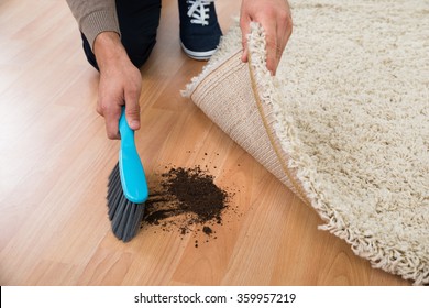 High angle view of man using brush to sweep mud on hardwood floor at home