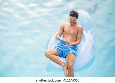 High angle view of man using digital tablet on inflatable ring at swimming pool - Powered by Shutterstock