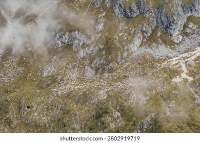 High angle view of a massive herd of sheep scattered across a steep, rocky mountain meadow partially covered by passing clouds in the Dolomites, Italy.