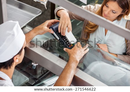 High angle view of mature female customer paying through smartphone at butchery