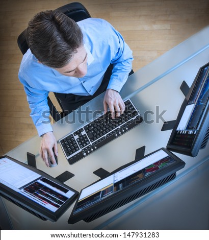 High angle view of mature male trader analyzing data on multiple screens at desk in office
