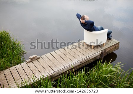 High angle view of mature man with hands behind head relaxing on chair at pier